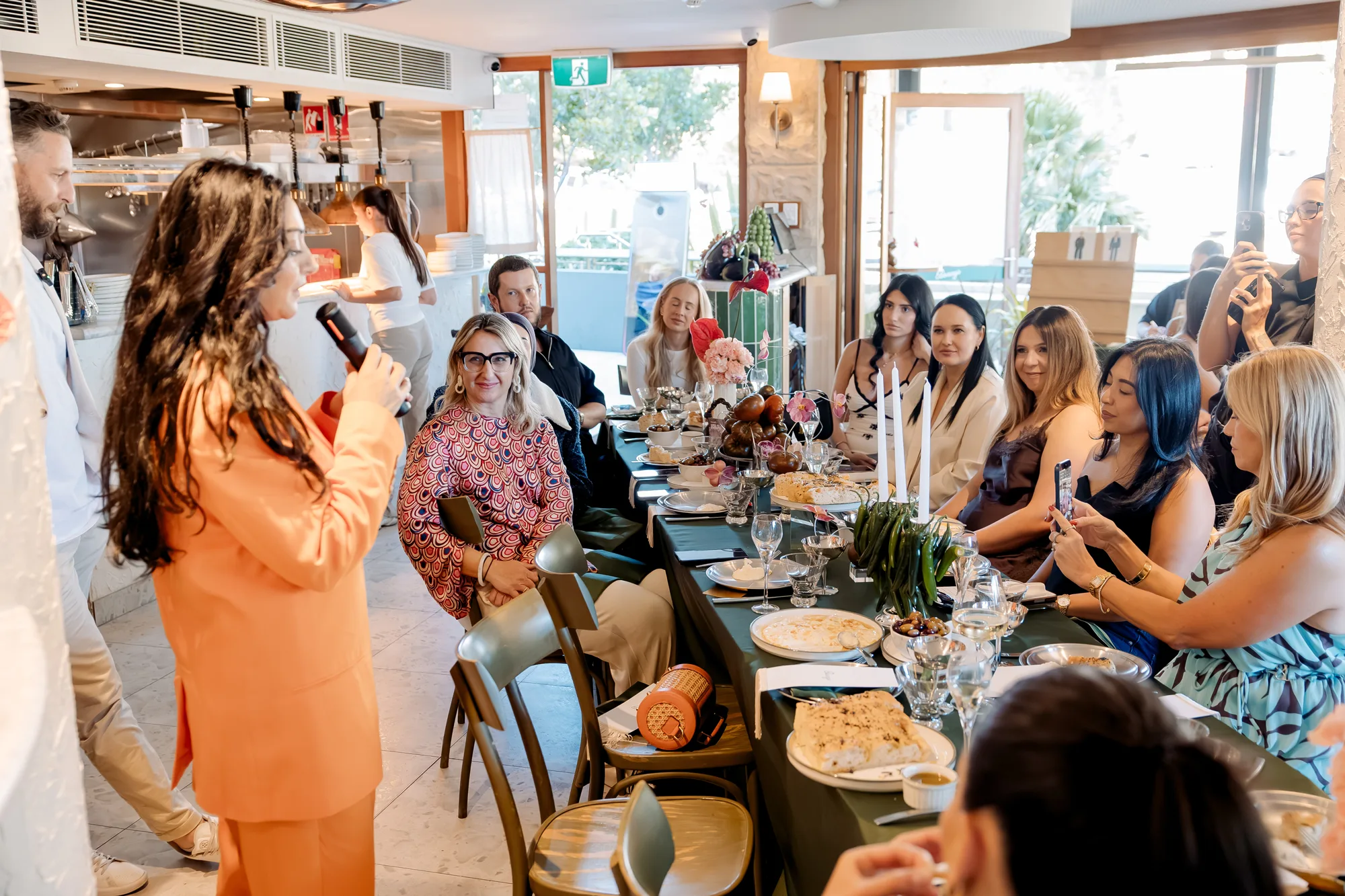 A host addressing guests seated at a long lunch table at Wedded Connect