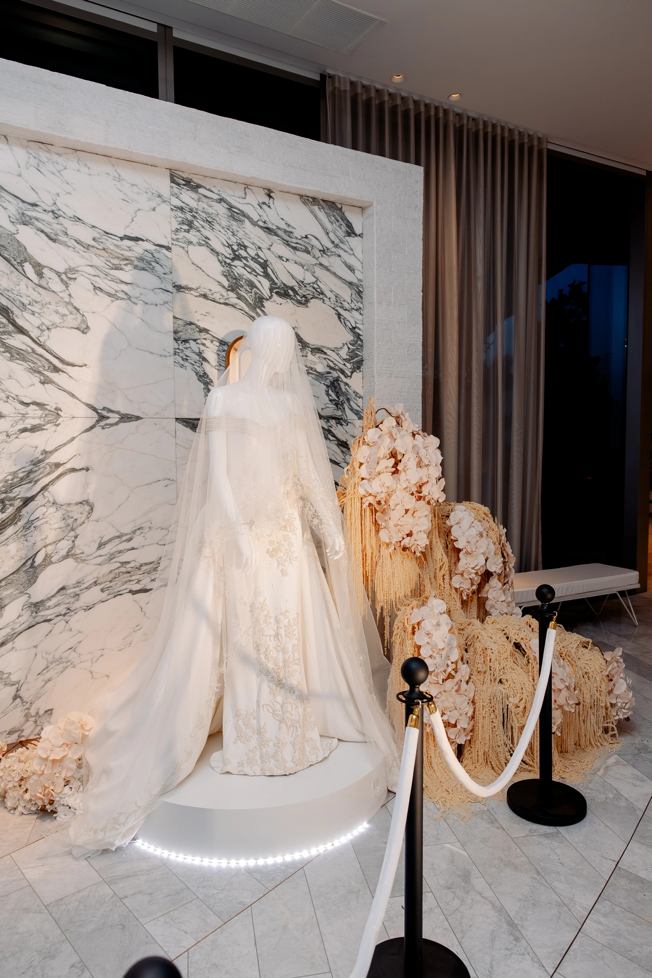 A couture gown displayed on a lit plinth beside a floral installation at Wedded World