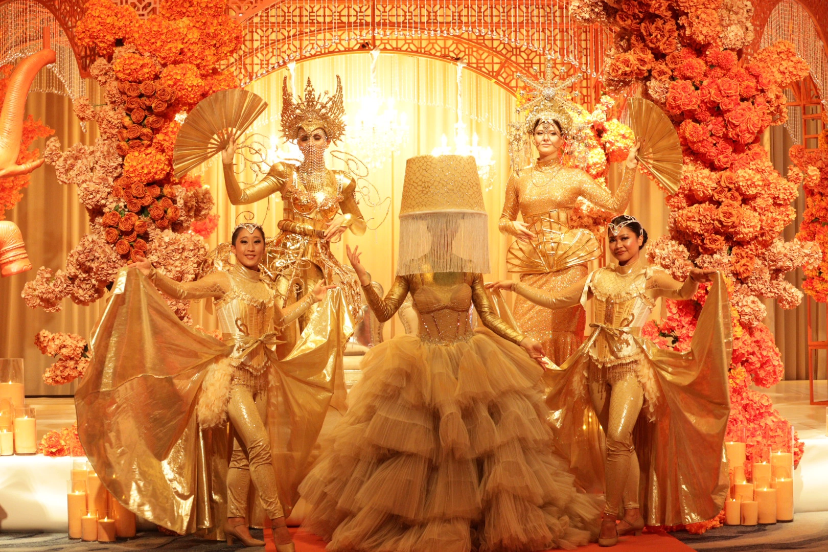 Gold-costumed performers before a floral arch in a themed designer space at Wedded World